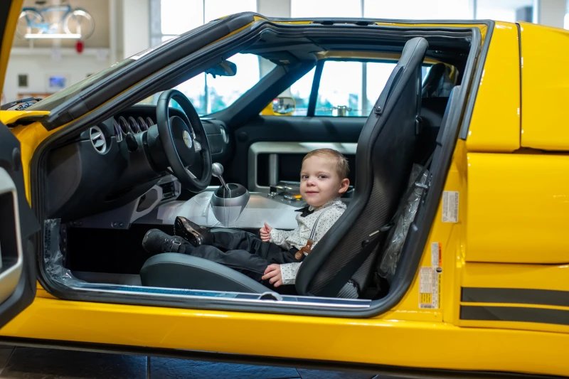 boy sitting in drivers seat of yellow race car